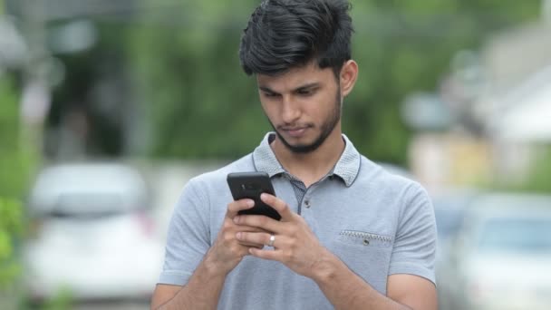 Молодой счастливый бородатый индиец пользуется телефоном на открытом воздухе — стоковое видео