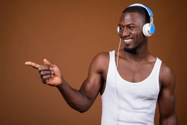 Hombre africano musculoso guapo escuchando música contra marrón b —  Fotos de Stock