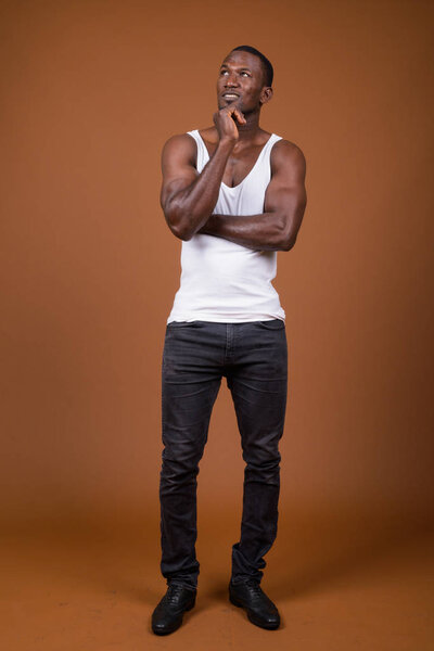 Studio shot of handsome muscular African man wearing tank top against brown background