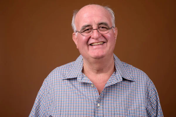 Hombre mayor con sobrepeso que usa anteojos contra fondos marrones —  Fotos de Stock