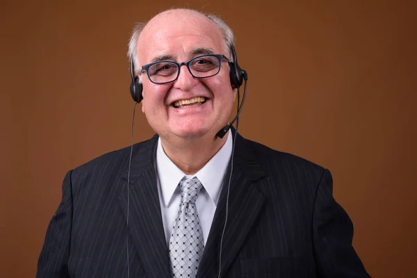 Overweight senior businessman wearing eyeglasses against brown b