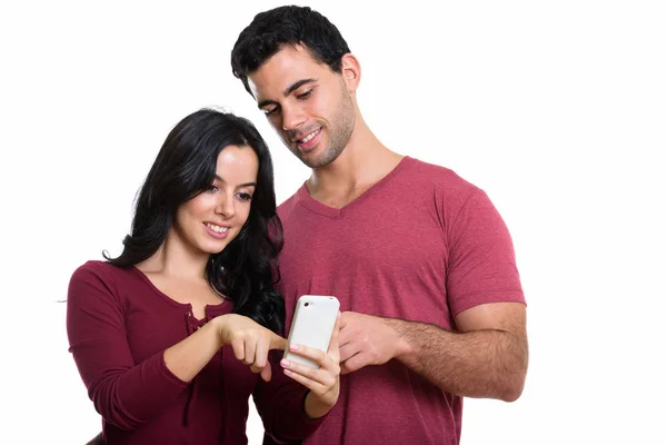 Studio shot of young happy couple smiling while using one mobile — Stock Photo, Image