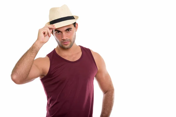 Studio shot of young handsome Hispanic man holding hat on head — Stock Photo, Image