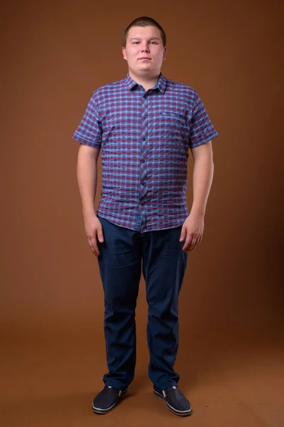 Studio záběr obézní mladík proti hnědým pozadím — Stock fotografie