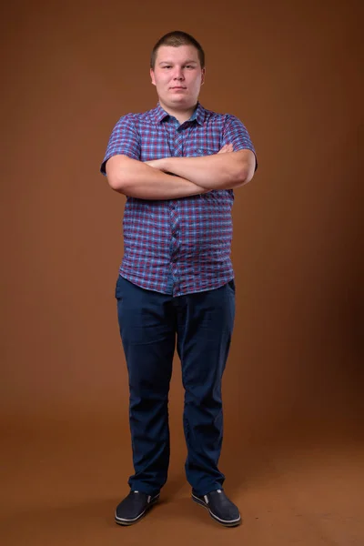Studioaufnahme eines übergewichtigen jungen Mannes vor braunem Hintergrund — Stockfoto
