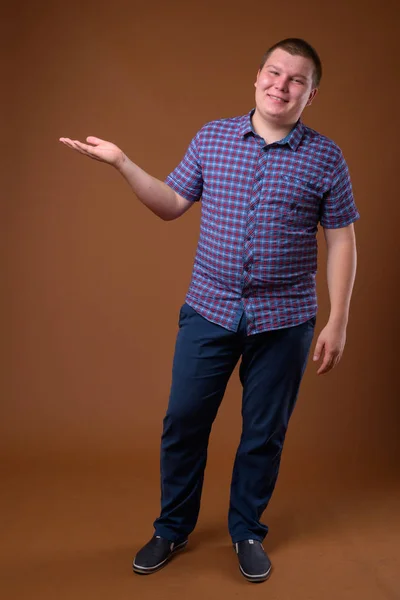 Studioaufnahme eines übergewichtigen jungen Mannes vor braunem Hintergrund — Stockfoto