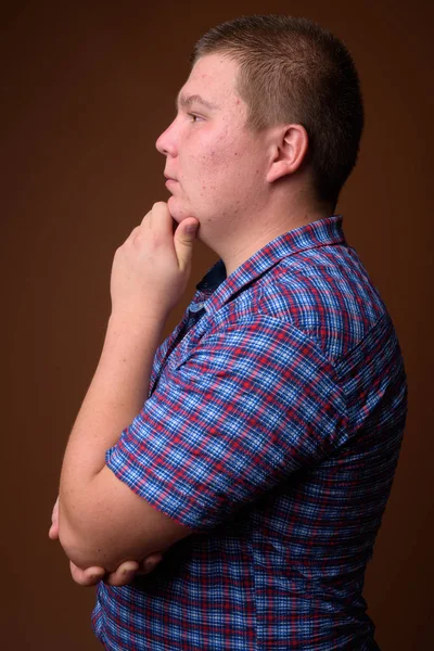 Studio shot of overweight young man against brown background — Stock Photo, Image