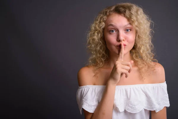 Ung vacker kvinna med blont lockigt hår mot grå backgro — Stockfoto