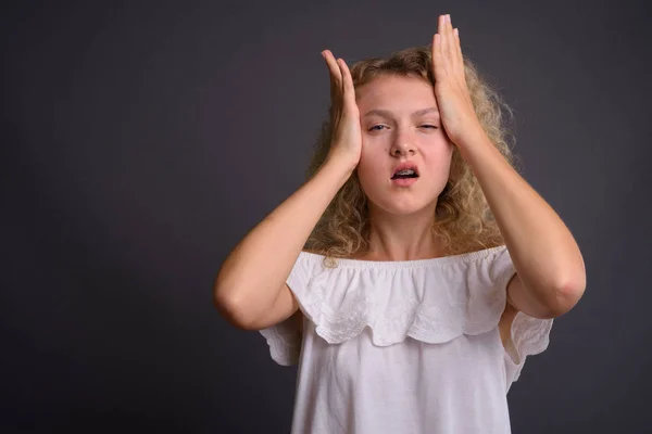 Ung vacker kvinna med blont lockigt hår mot grå backgro — Stockfoto