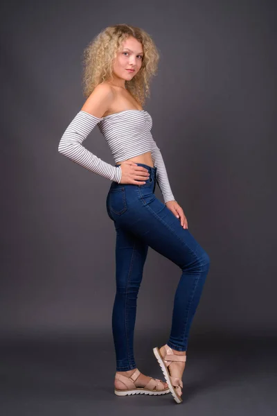 Junge schöne Frau mit blonden lockigen Haaren gegen grauen Backgro — Stockfoto