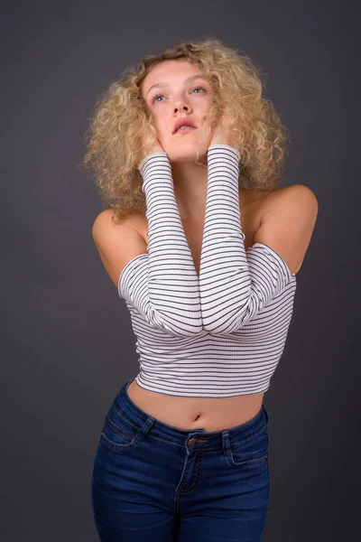 Ung vacker kvinna med blont lockigt hår mot grå backgro — Stockfoto