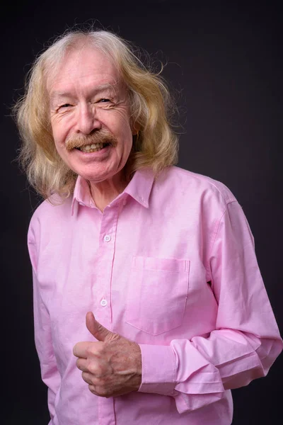 Senior businessman wearing pink shirt against gray background — Stock Photo, Image