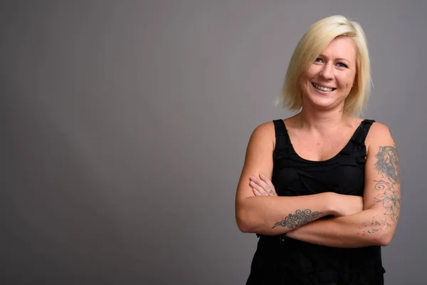 Portrait of woman with blond hair smiling against gray background — Stock Photo, Image