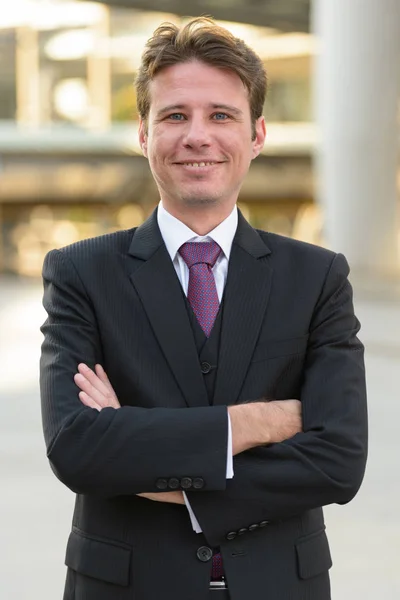 Feliz hombre de negocios sonriendo con los brazos cruzados delante de la moderna b — Foto de Stock