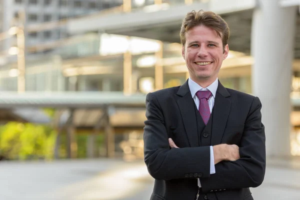 Feliz hombre de negocios sonriendo con los brazos cruzados delante de la moderna b — Foto de Stock