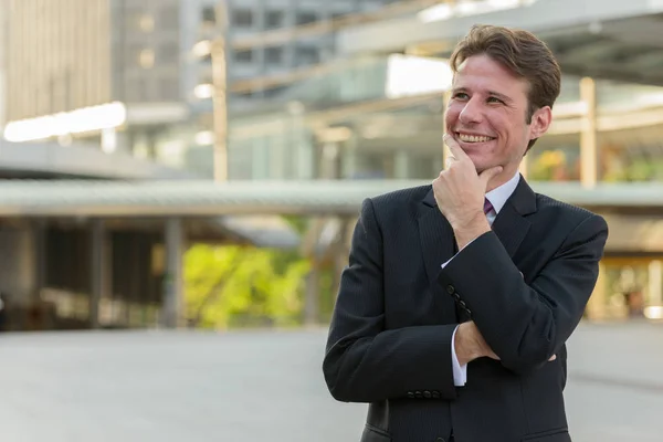 Feliz hombre de negocios sonriendo y pensando en frente de buildi moderno — Foto de Stock