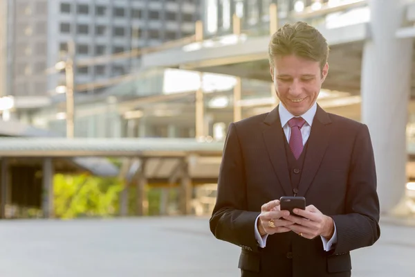 Happy businessman smiling and using mobile phone in front of mod — Stock Photo, Image