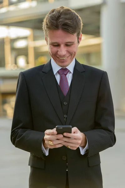 Homme d'affaires heureux souriant et utilisant le téléphone mobile devant mod — Photo