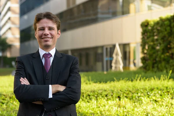 Feliz hombre de negocios sonriendo con los brazos cruzados delante de g moderno — Foto de Stock