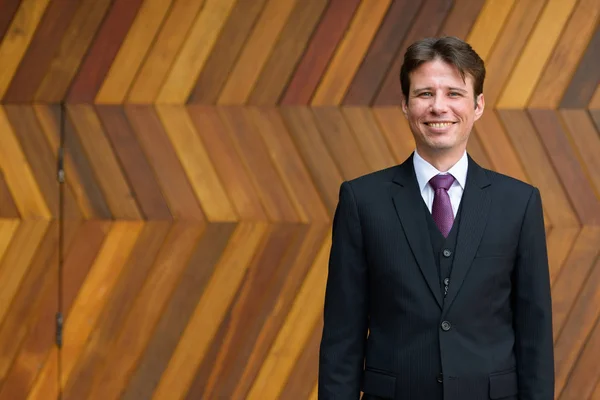 Feliz hombre de negocios sonriendo contra zigzag modelado pared de madera al aire libre — Foto de Stock