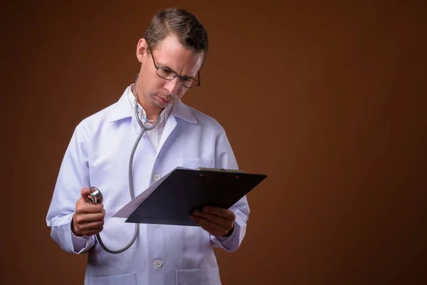 Studio shot of man doctor against brown background — Stock Photo, Image