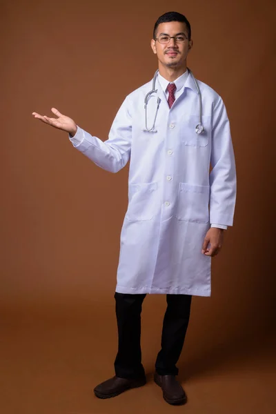 Młody człowiek Asian wieloetnicznego lekarz na brązowym tle — Zdjęcie stockowe