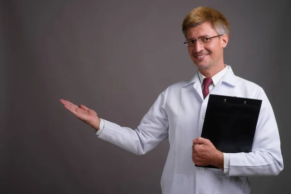 Doktor muž s blond vlasy proti šedé pozadí — Stock fotografie