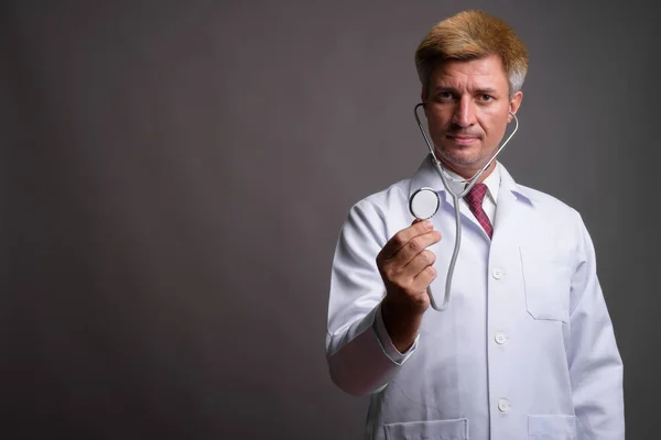 Doktor muž s blond vlasy pomocí stetoskopu proti šedé pozadí — Stock fotografie