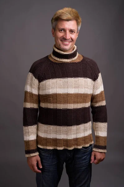 Hombre con el pelo rubio usando suéter de cuello alto contra la espalda gris —  Fotos de Stock