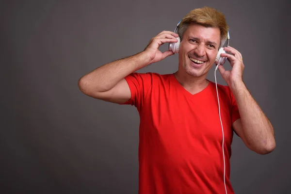 Мужчина с светлыми волосами слушает музыку на сером фоне — стоковое фото