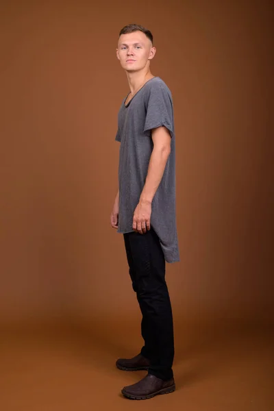 Молодой человек в серой рубашке на коричневом фоне — стоковое фото