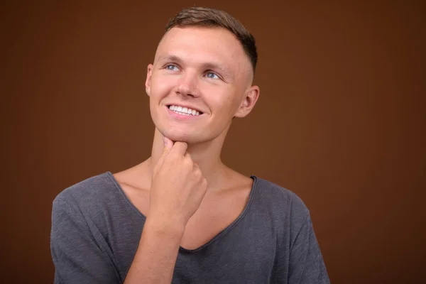 Junger Mann mit grauem Hemd vor braunem Hintergrund — Stockfoto