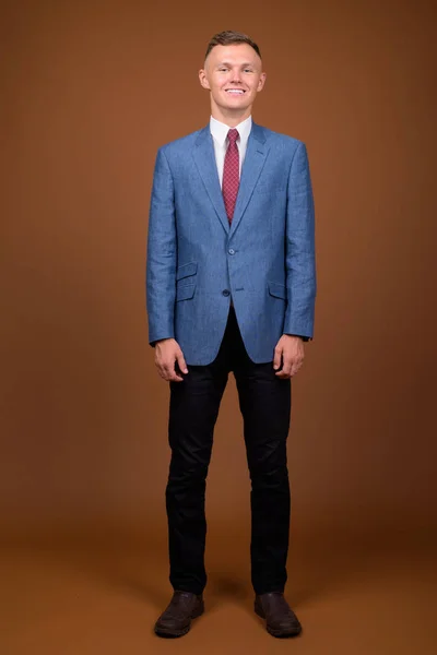 Νεαρός επιχειρηματίας φορώντας κοστούμι ενάντια σε καφέ φόντο — Φωτογραφία Αρχείου