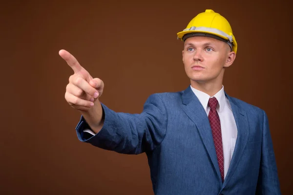 Young businessman wearing hardhat against brown background — Stock Photo, Image