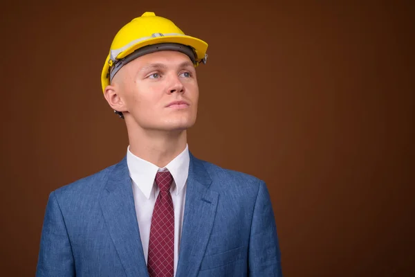 Joven hombre de negocios vistiendo hardhat contra fondo marrón —  Fotos de Stock