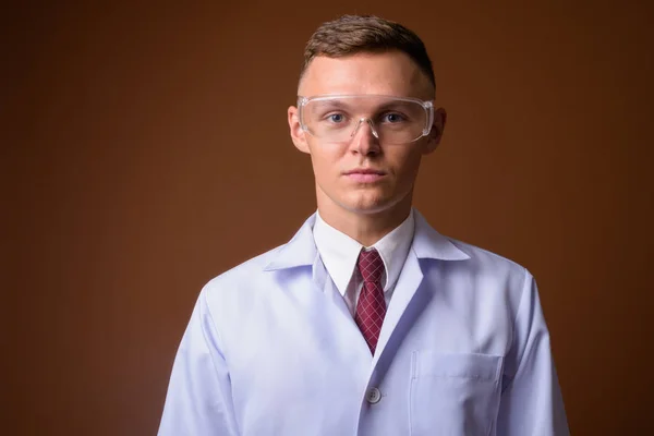 Joven doctor con gafas protectoras contra el marrón backgr —  Fotos de Stock