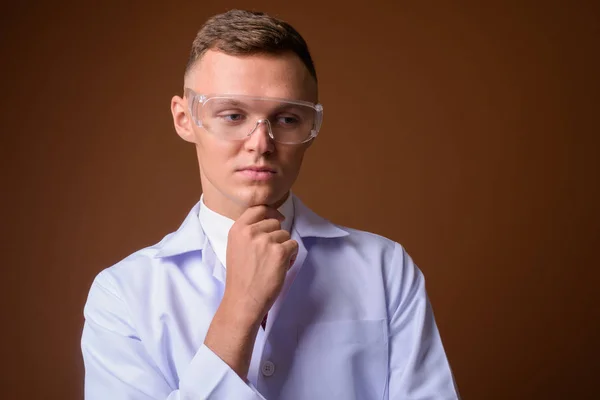 Молодий чоловік лікар в захисних окулярах проти коричневого ременя — стокове фото