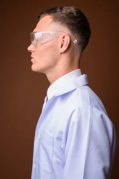 Joven doctor con gafas protectoras contra el marrón backgr —  Fotos de Stock