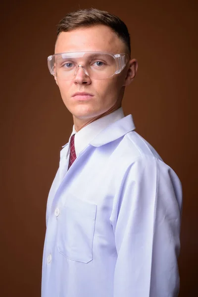 Młody człowiek lekarza okularów ochronnych przeciwko brązowym tle — Zdjęcie stockowe