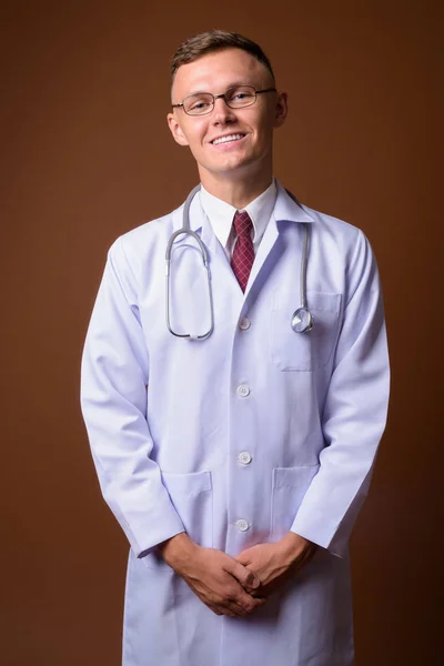 Joven doctor vistiendo anteojos sobre fondo marrón —  Fotos de Stock