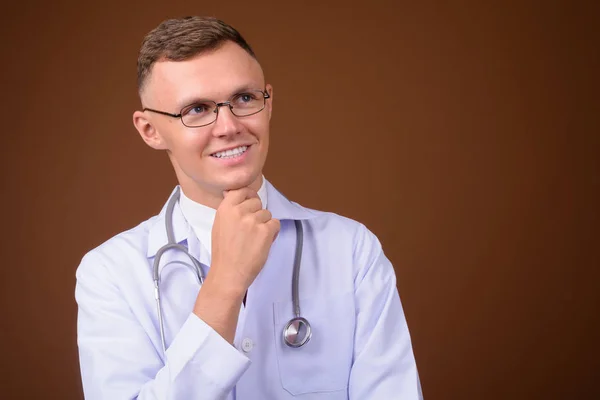 Jeune homme médecin portant des lunettes sur fond brun — Photo