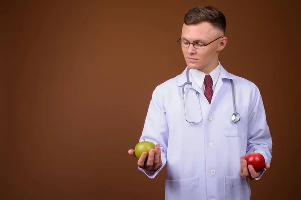 Jovem médico vestindo óculos contra fundo marrom — Fotografia de Stock