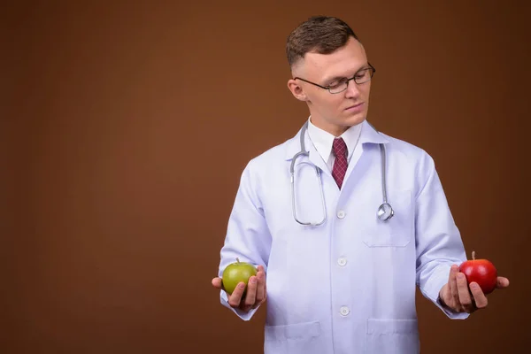 Joven doctor vistiendo anteojos sobre fondo marrón —  Fotos de Stock