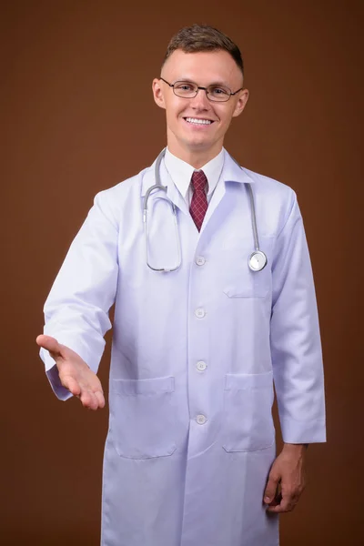 Jovem médico vestindo óculos contra fundo marrom — Fotografia de Stock