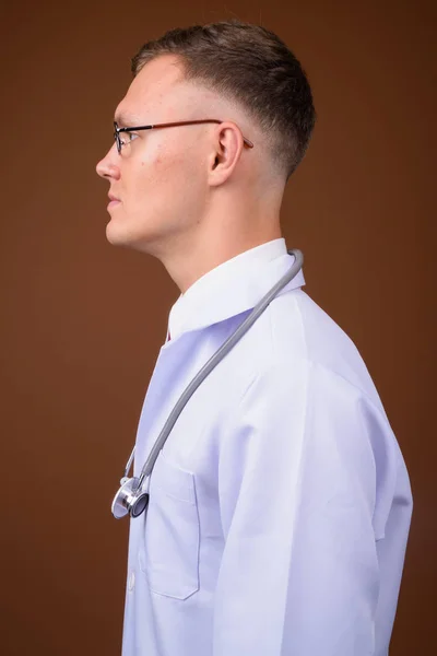 Fiatal férfi orvos visel szemüveget barna háttér — Stock Fotó