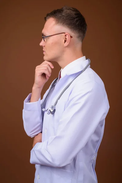 Jeune homme médecin portant des lunettes sur fond brun — Photo