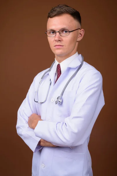 Молодий лікар носить окуляри на коричневому фоні — стокове фото