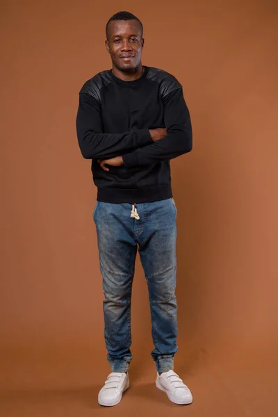 Studio shot of young African man against brown background — Stock Photo, Image