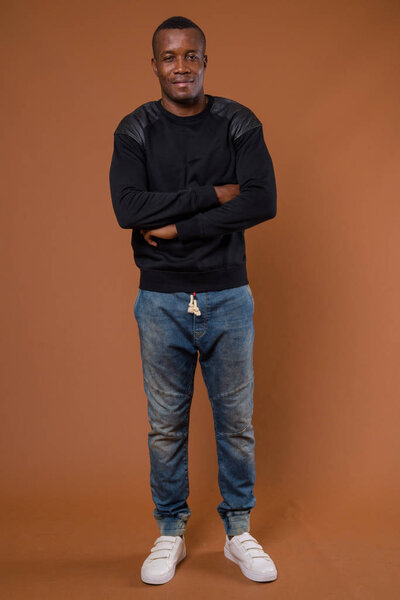 Studio shot of young African man wearing black long sleeved shirt against brown background