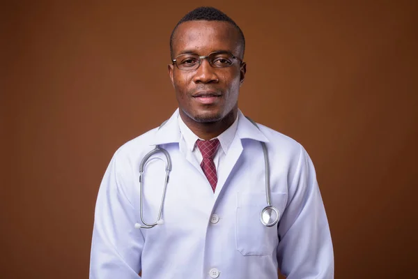 Estúdio tiro de jovem médico homem africano contra fundo marrom — Fotografia de Stock